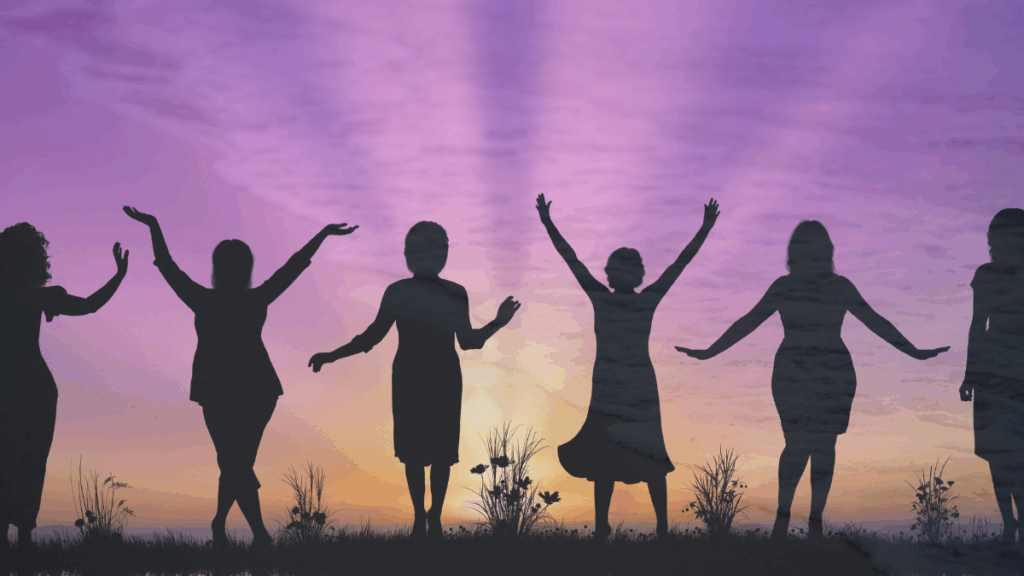 Silhouettes of diverse women standing together with open arms against a purple and gold sunset sky, symbolizing confidence, unity, and empowerment after 40.