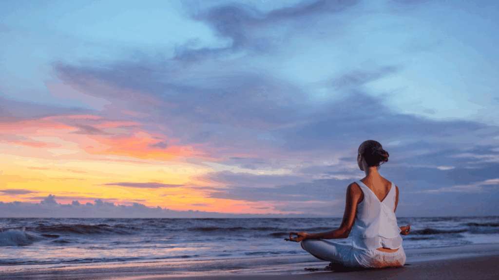 Woman meditating on the beach at sunrise, symbolizing peace and happiness by choice