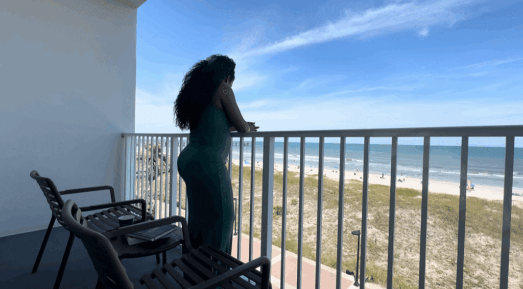 Woman standing on a balcony overlooking the ocean, reflecting on courage and new beginnings.