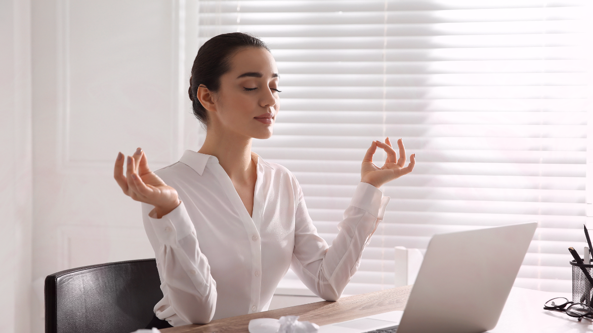 Woman meditating calmly at her desk with soft natural light, symbolizing balance, focus, and inner peace.
